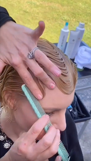 Finger waves: mulher branca, de cabelos loiros, fazendo ondas nos seus fios com um pente azul bebê.