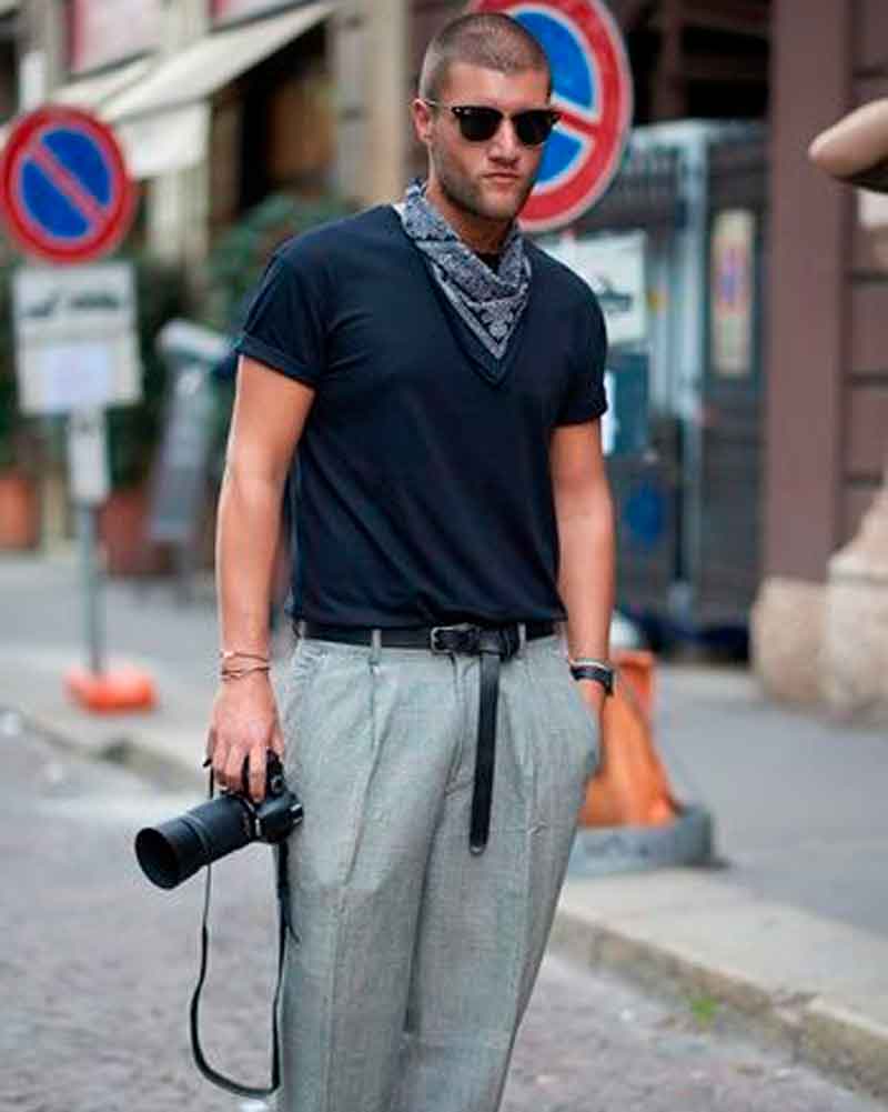 Homem fotógrafo streetslytile estilo de rua com calça cinza, camiseta azul, lenço azul e óculos de sol, segurando uma câmera profissional