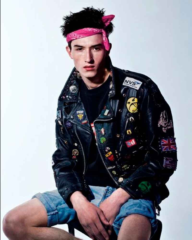 Homem jovem com estilo punk, jaqueta de couro com pin, shorts jeans, camiseta preta e bandana rosa estilo Fiuk BBB21
