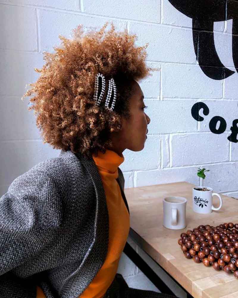 Mulher negra em uma cafeteria com cabelo curto crespo penteado para transição capilar com presilhas