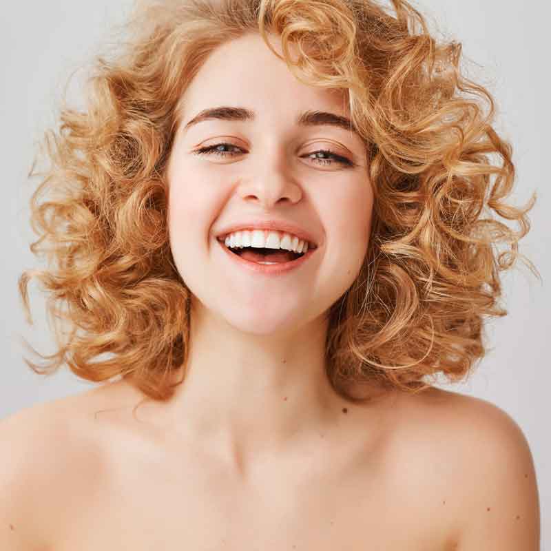 Mulher branca com cabelo cacheado loiro sorrindo para a câmera