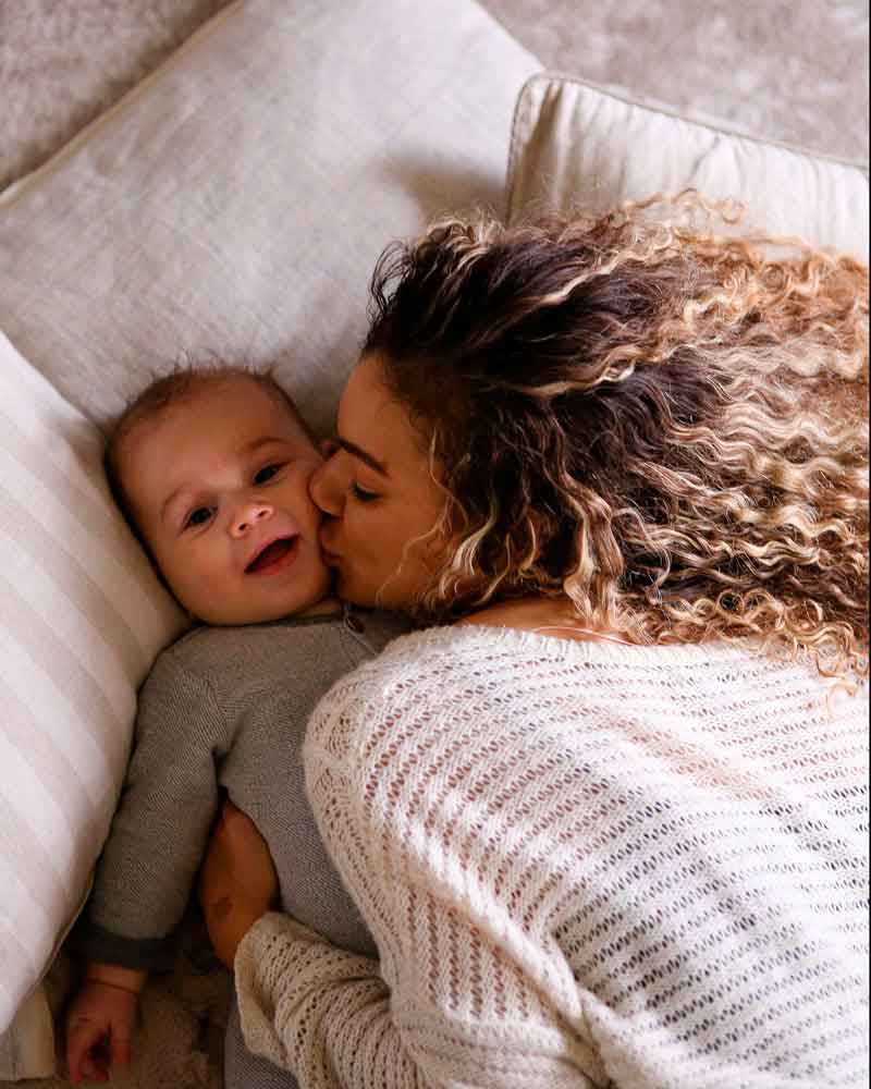 Mulher mãe de filho pequeno com cabelo cacheado longo natural abraçando, sorrindo e brincando com bebê