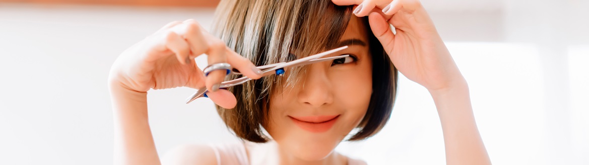 Jovem asiática de cabelo chanel liso segurando uma tesoura e aprendendo como cortar o cabelo sozinha