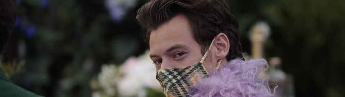 Harry Styles sorrindo para a câmera no Grammy 2021 com máscara combinando com o terno, pluma lilás e cabelo querubim