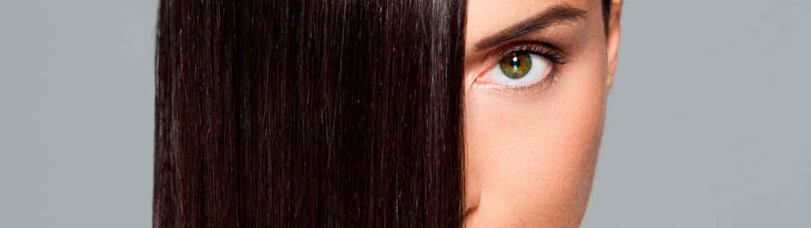 Mulher de olhos verdes com cabelo castanho liso e brilhante após botox capilar, olhando para a câmera em fundo neutro