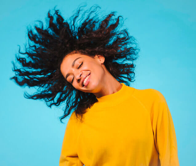 mulher sorridente de roupa amarela e cabelo ao vento em um fundo azul